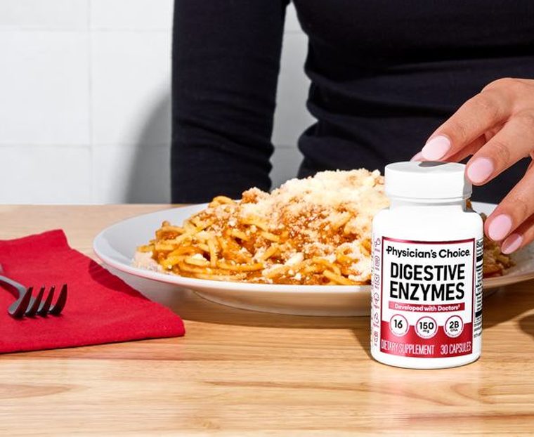 A plate of spaghetti on a table, with a hand reaching for a bottle of Physician's Choice Digestive Enzymes